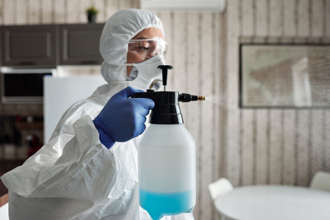 Services-03 Professional in full gear disinfecting indoor area using a spray bottle for COVID-19 prevention.
