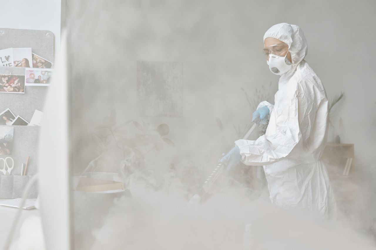 why-choose-us A woman in a protective suit disinfects an indoor space with fogging equipment.